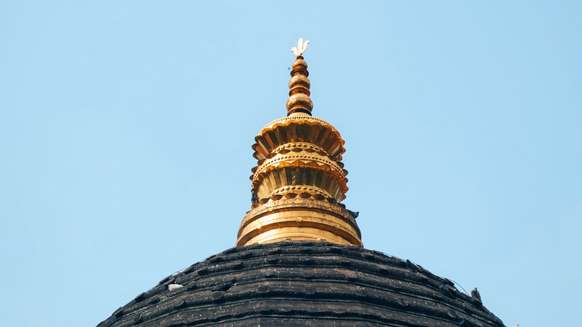 Close up view of a temple dome structure featuring a decorative spire, textured surface, clear sky in the background.