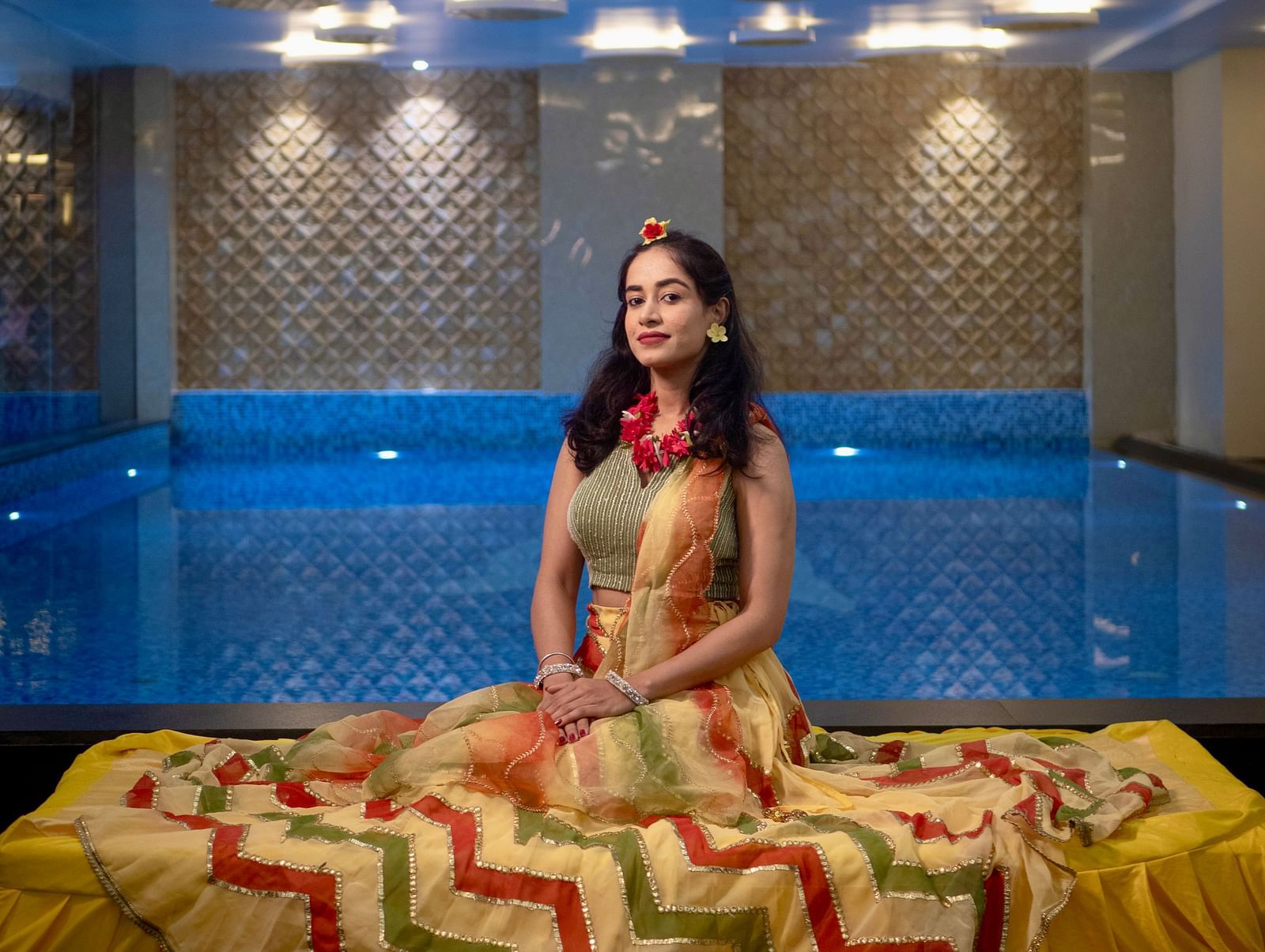 Woman seated by the pool in traditional attire with blue lighting at Mansha Regency, Port Blair.