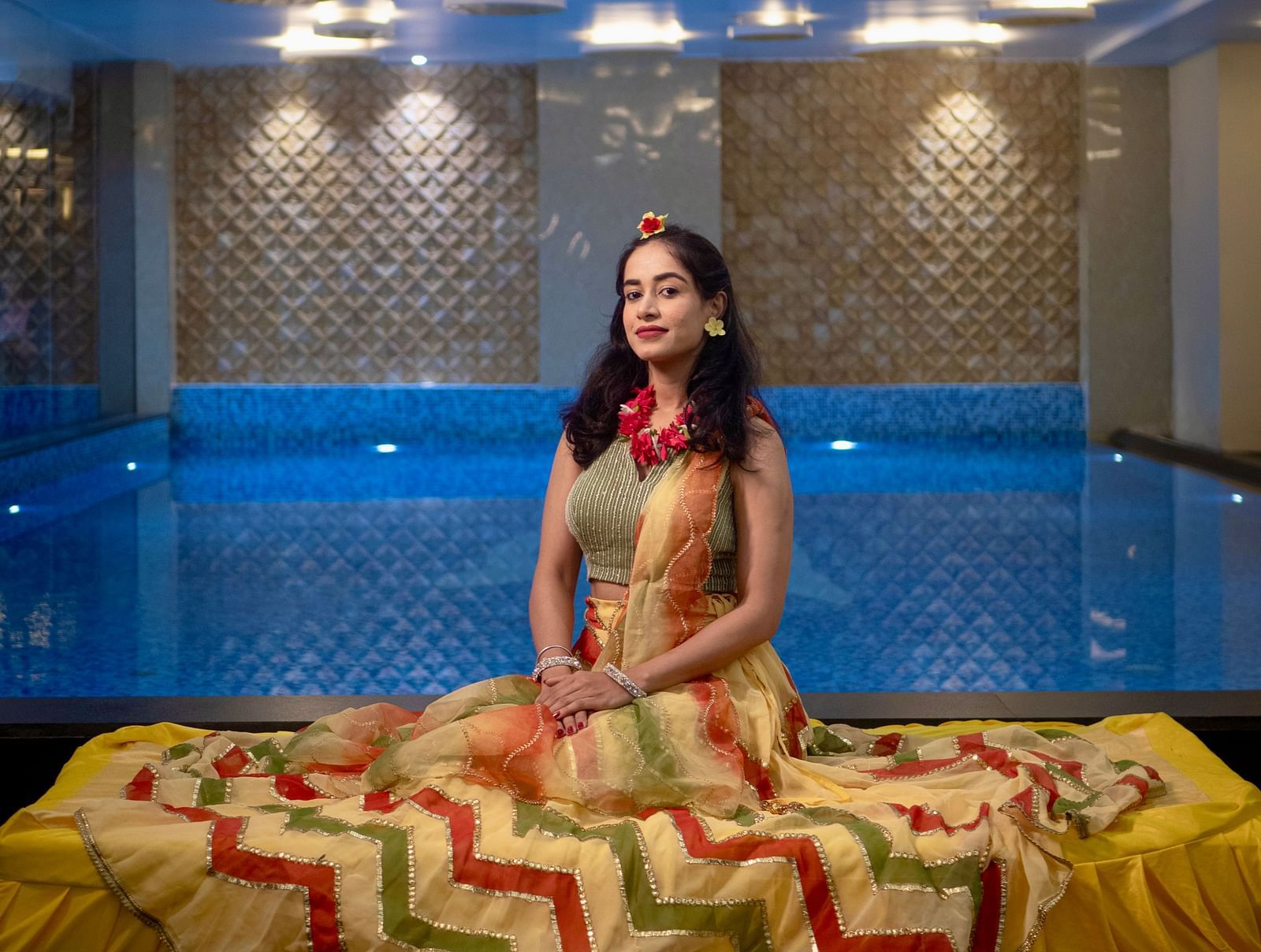 Woman seated by the pool in traditional attire with blue lighting at Mansha Regency, Port Blair.
