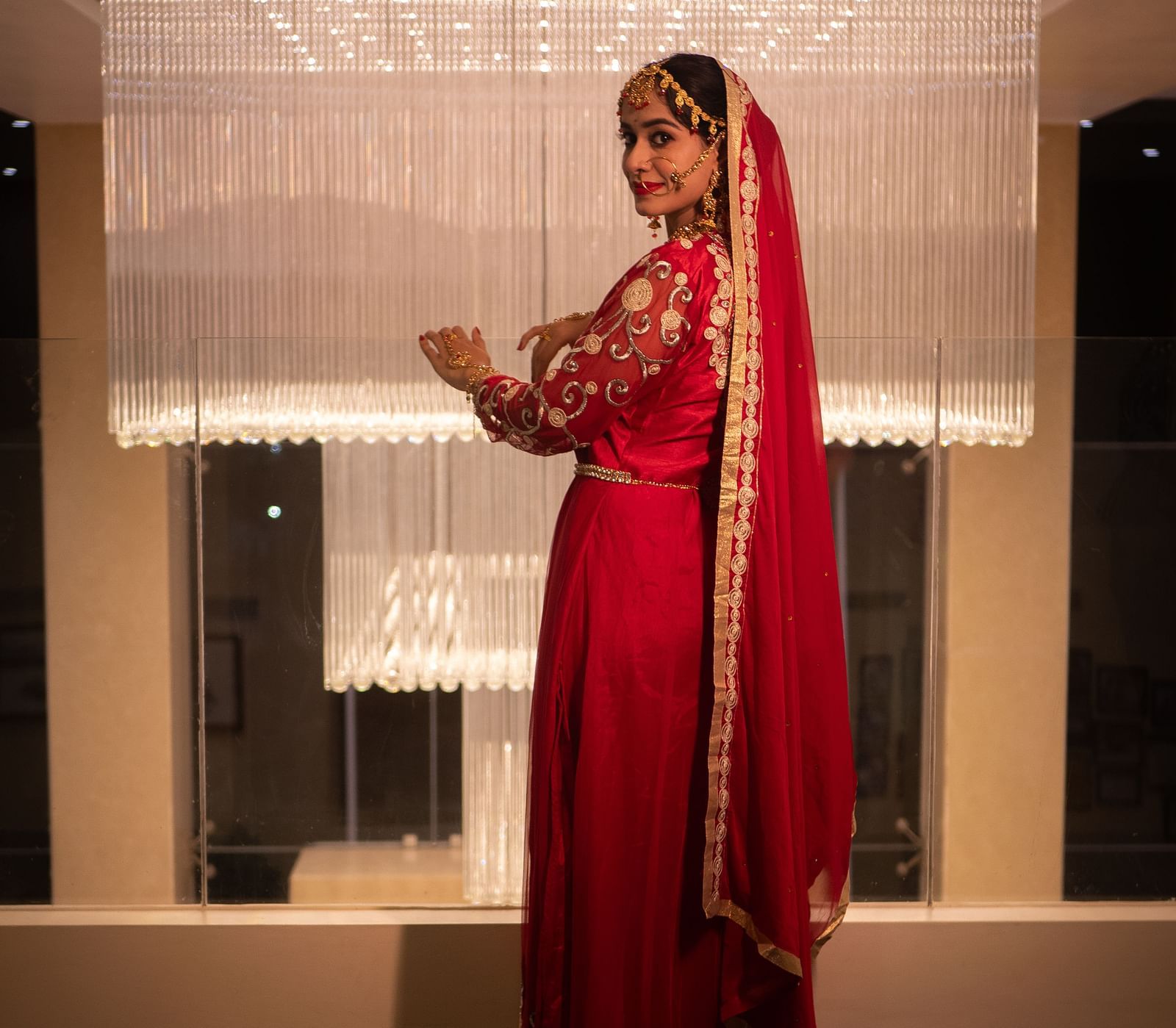 Bride in red outfit standing in a suite near a window at Mansha Regency, Port Blair.