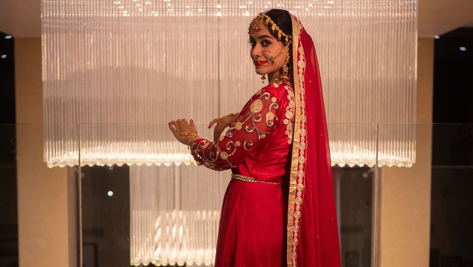 Bride in red outfit standing in a suite near a window at Mansha Regency, Port Blair.