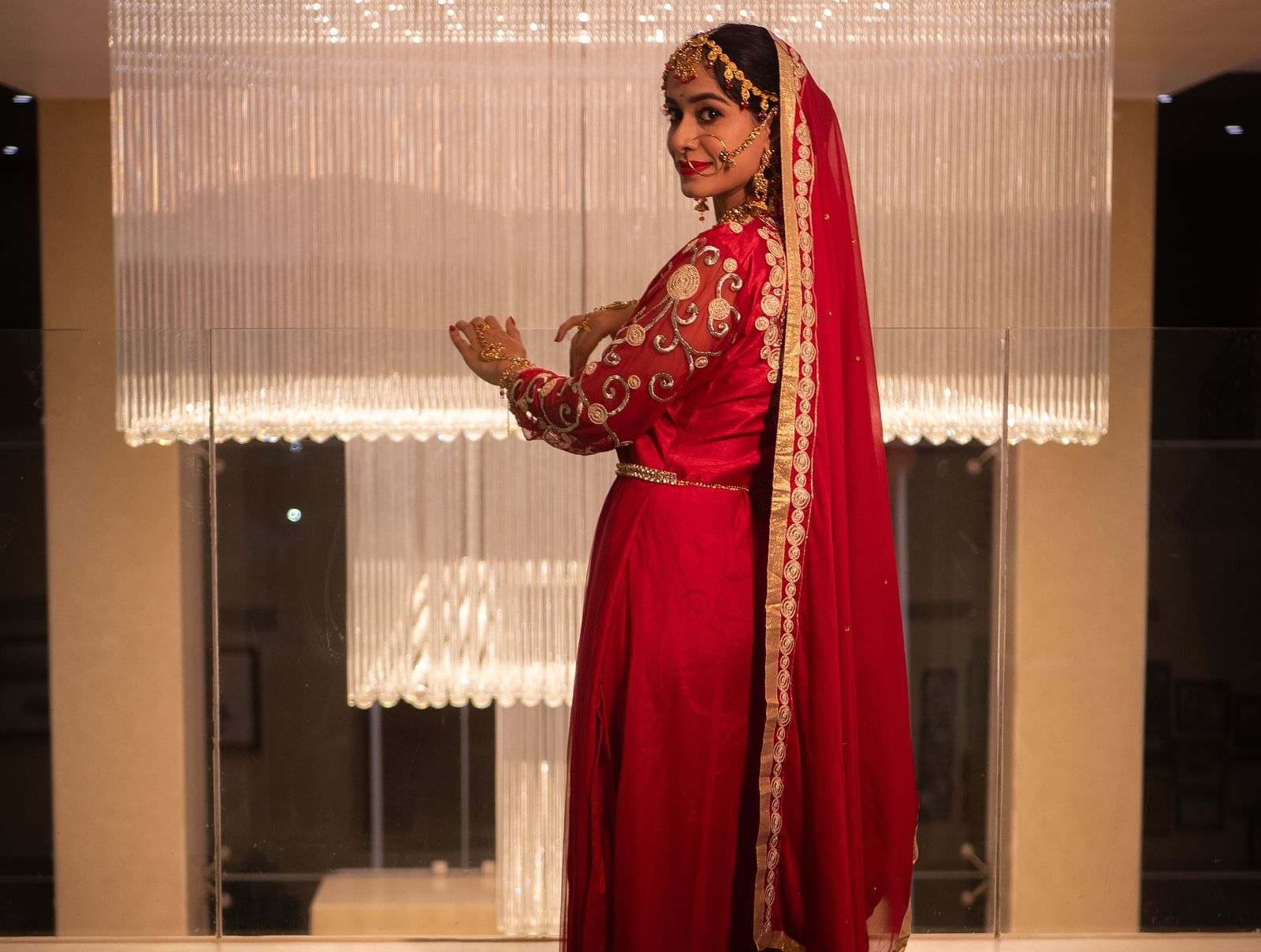 Bride in red outfit standing in a suite near a window at Mansha Regency, Port Blair.