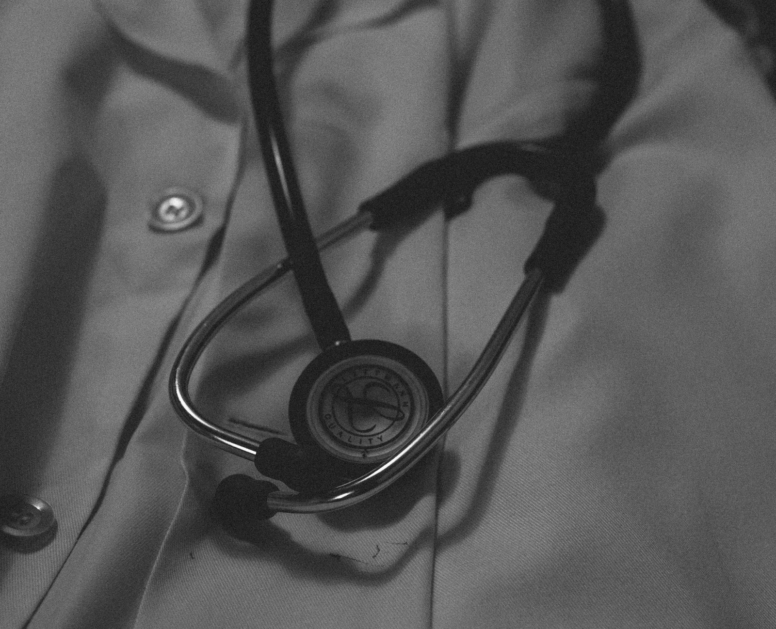 A black and white photo of a stethoscope resting on top of a doctor's lab coat.