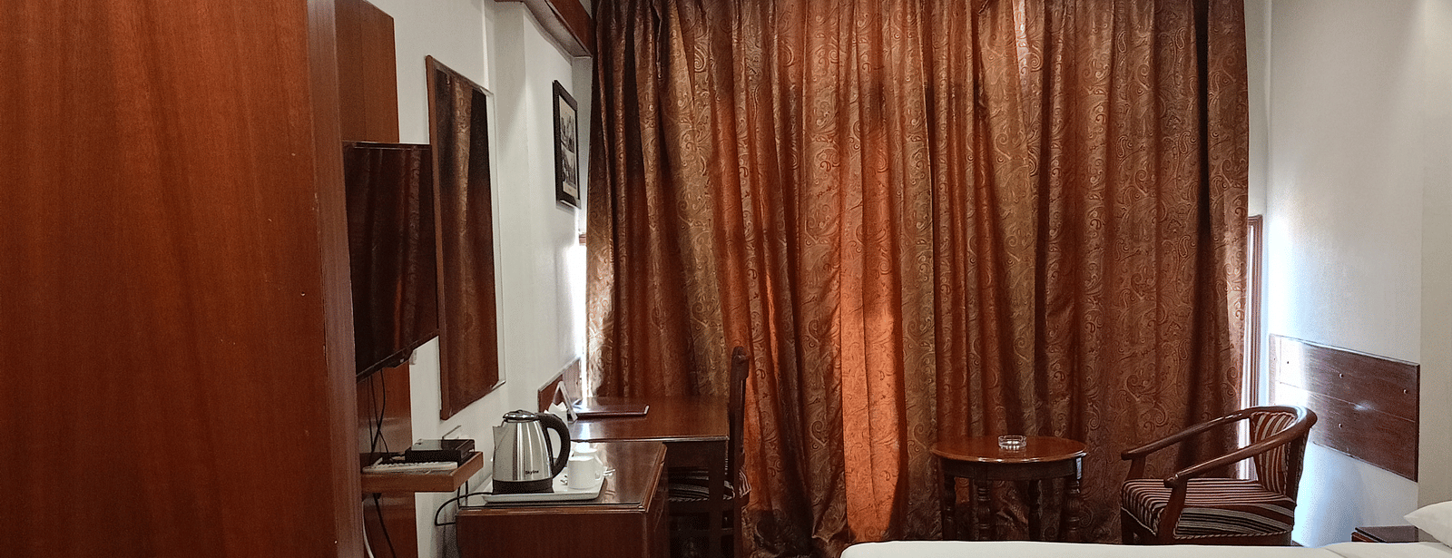 Guest room at Hotel Gold, Panipat showing a bed, curtains, and a desk along the side wall.