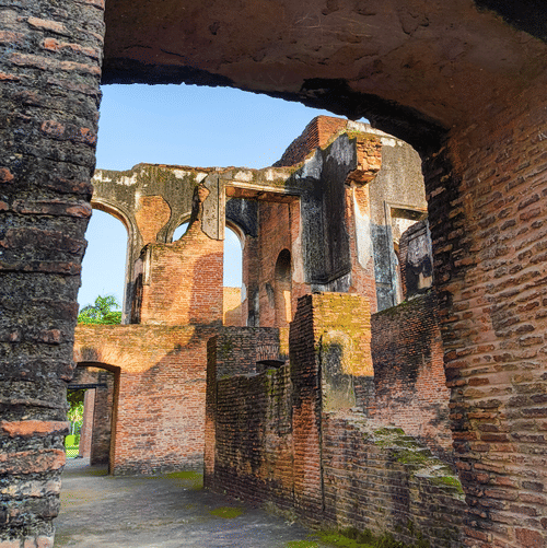 A view of the moss covered walls of The Residency, Lucknow, through one of the arched doors.  The tall walls are visible through the doorway.