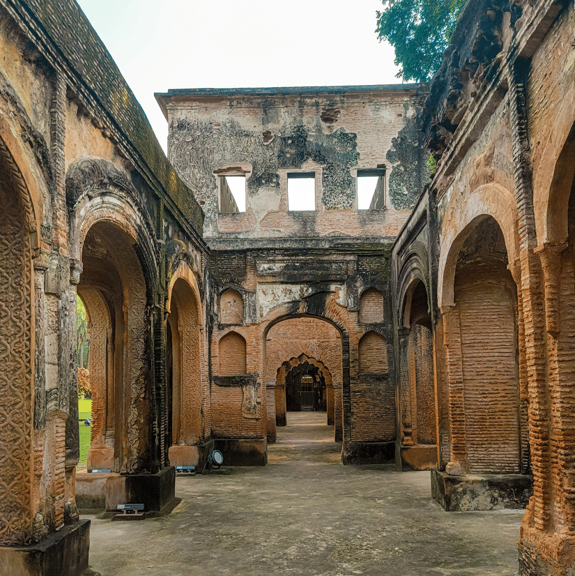 A open hallway at The Residency, Lucknow. It has arch doorways framing it from both sides while one of the walls in the front rise up to a second storey.