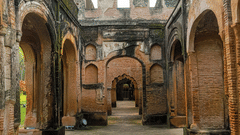 A open hallway at The Residency, Lucknow. It has arch doorways framing it from both sides while one of the walls in the front rise up to a second storey.