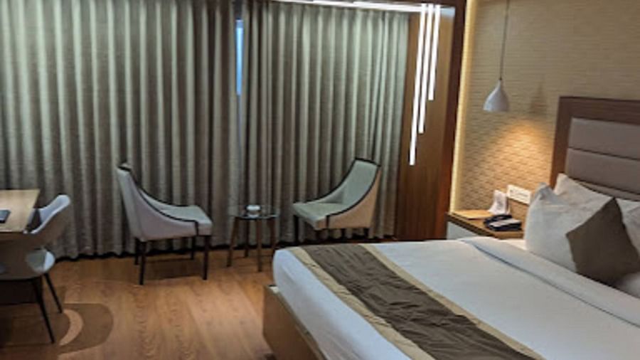 A premium hotel room with a neatly made large bed, windows with closed curtains, along with two chairs at Yashshree The Imperial Inn, Siliguri.