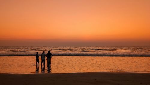 A group of people standing at the beach at sunset