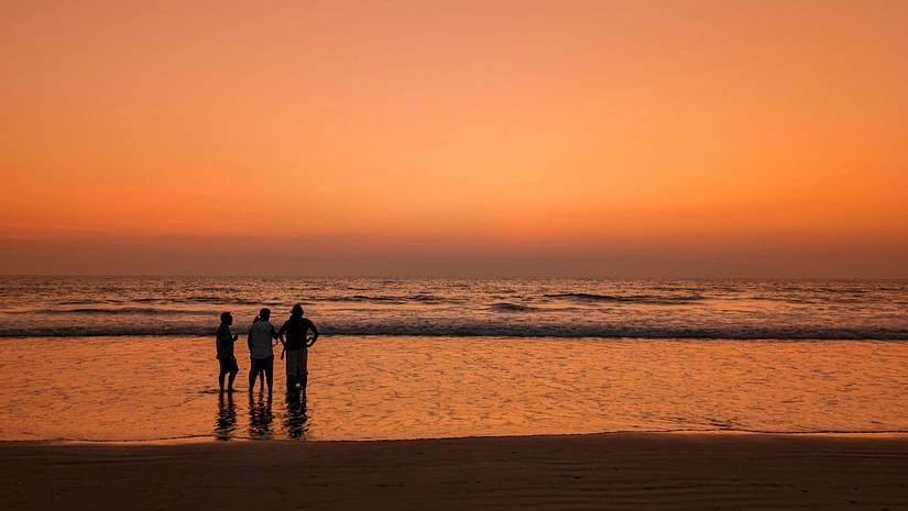 A group of people standing at the beach at sunset
