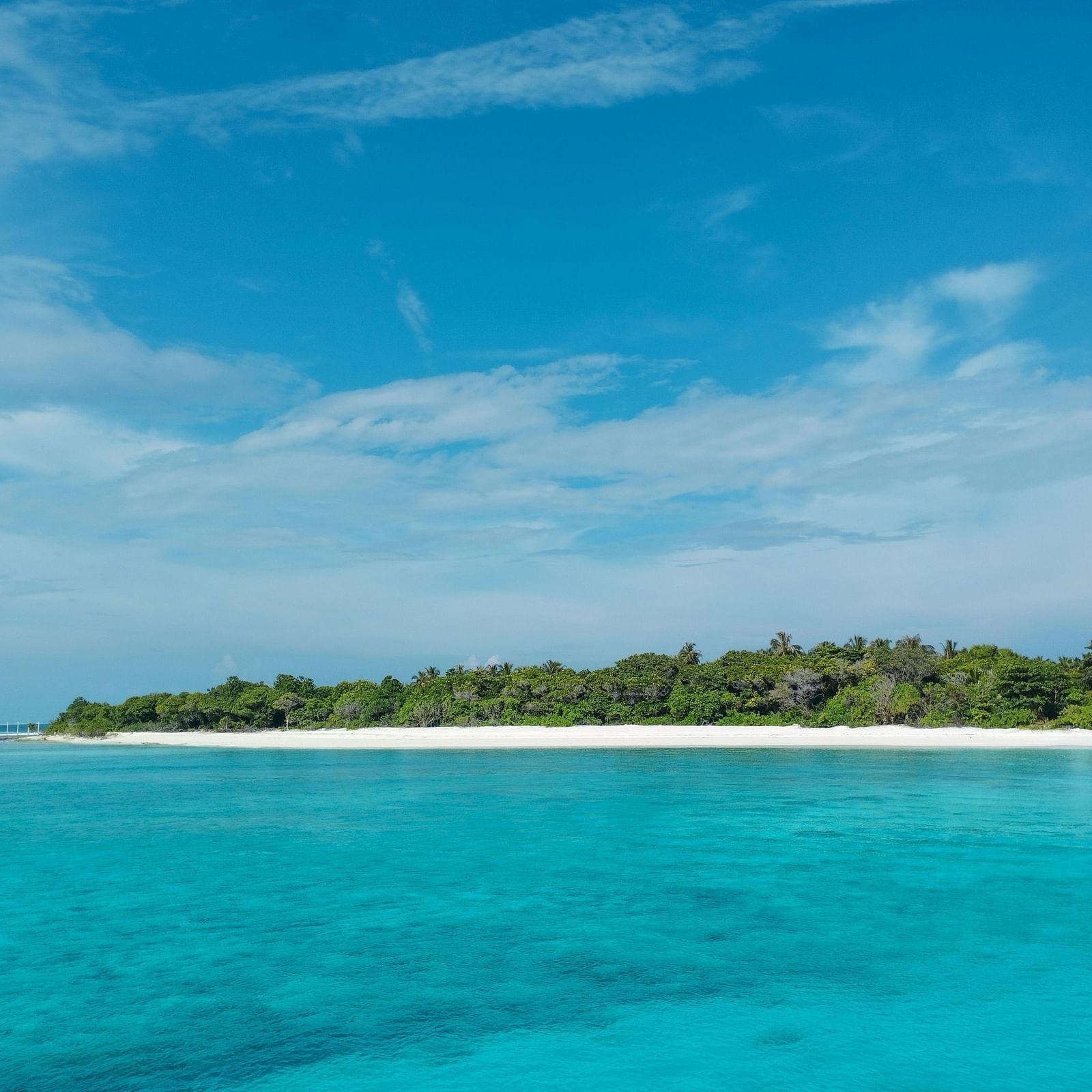 A pristine tropical island with white sandy beaches and clear turquoise waters under a bright blue sky, offering a perfect paradise getaway.