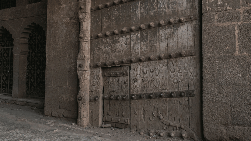 Massive wooden fort door reinforced with iron spikes beneath a tall stone archway.