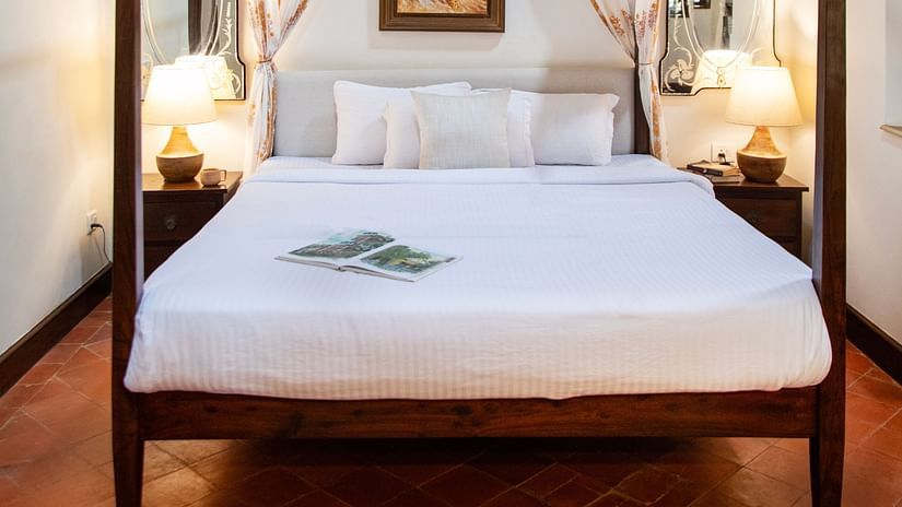 An image of a bedroom with poster beds and bedside table with lamp on either side -Lamrin Ucassaim Hotel, Goa