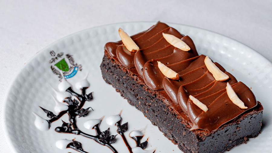 A chocolate brownie topped with slivered almonds at Café Latte, part of the Noor-Us-Sabah Palace, Bhopal, presented on a white plate with chocolate drizzle.