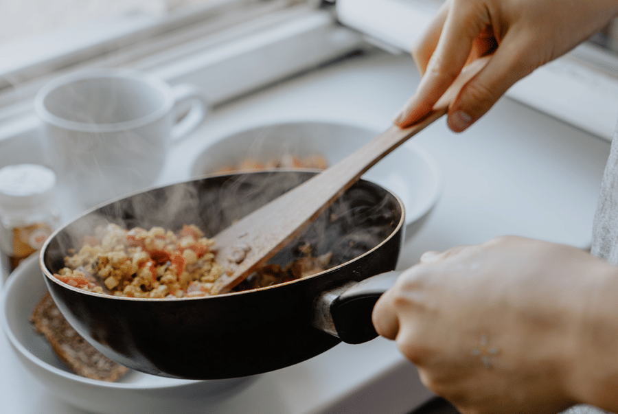 Hands stirring vegetables in a frying pan with a wooden spatula