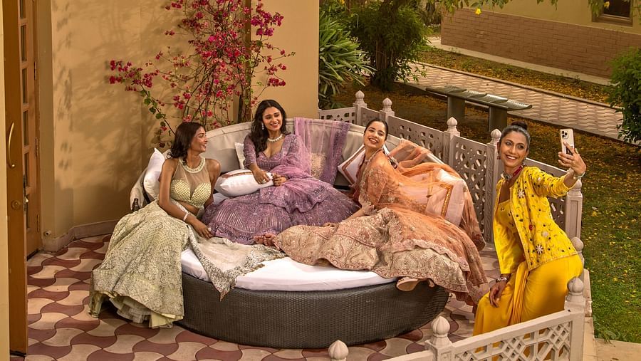 A group of women enjoying tea in a cozy garden setting with lush greenery, comfortable pillows, and ornate furniture at dusk.