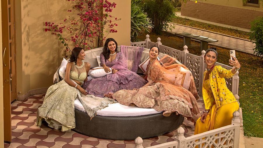 A group of women enjoying tea in a cozy garden setting with lush greenery, comfortable pillows, and ornate furniture at dusk.