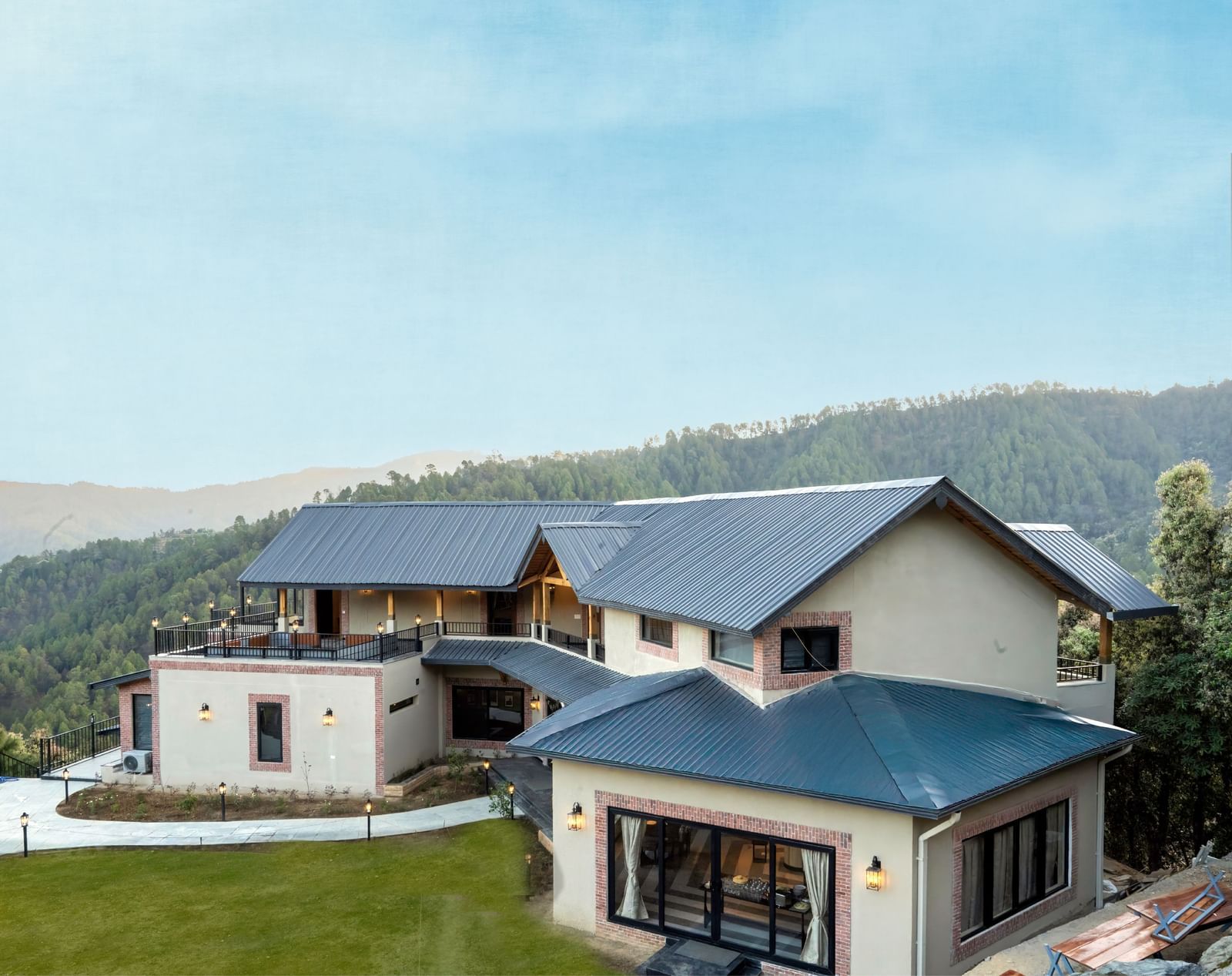 Long view of the façade of The Chamomile Estate with sloped roofs, set against lush hills under a clear sky.