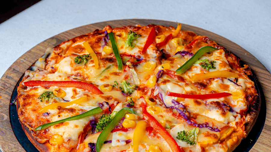 A vegetable pizza with peppers and onions at Café Latte, part of the Noor-Us-Sabah Palace, Bhopal, presented on a wooden serving board.