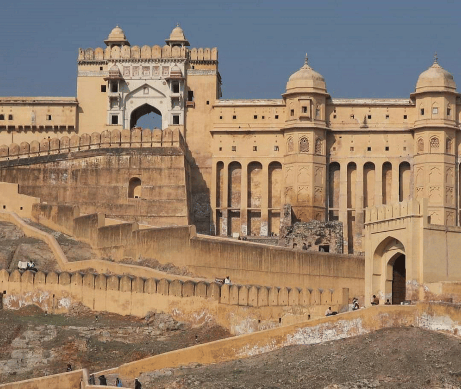 A large, ancient structure stands atop a hill, surrounded by defensive walls and sloping terrain.