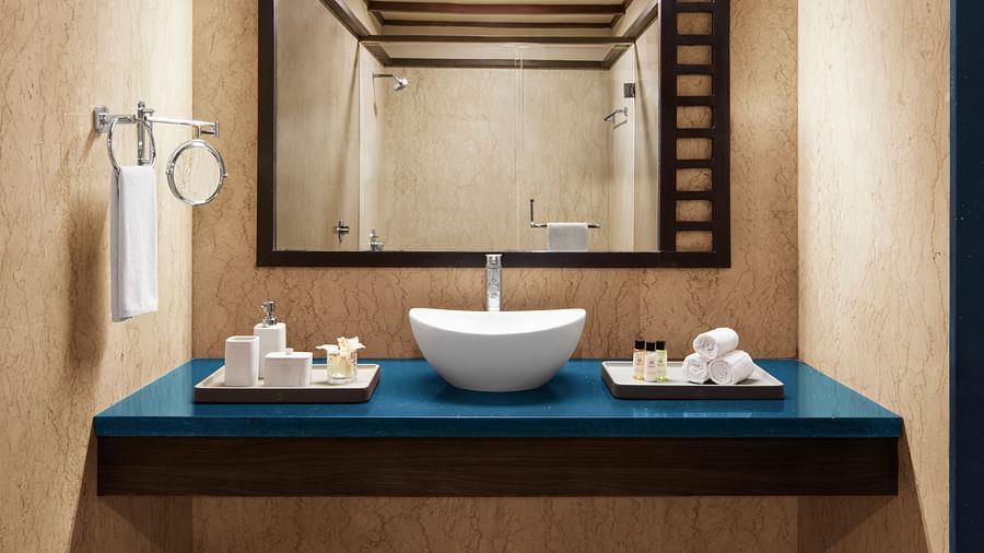 Bathroom of Executive Suite with a blue countertop, a white vessel sink, and a large mirror reflecting the room's warm lighting and wooden ceiling at DGV Resort by Treat, Silvassa.