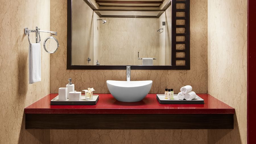 Bathroom of Signature Suite with a rectangular mirror, a white vessel sink, and red accents with toiletries at DGV Resort by Treat, Silvassa