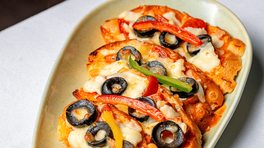 Cheesy bruschetta topped with black olives and peppers at Café Latte, part of the Noor-Us-Sabah Palace, Bhopal, served on an oval light-coloured plate.