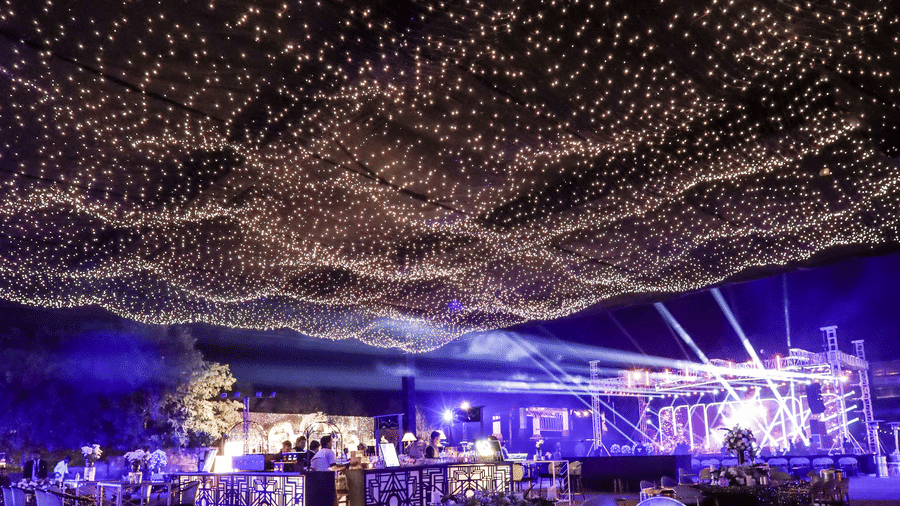 An enchanting night event setup at Ananta Spa & Resort, Jaipur, is covered by a wave-like ceiling canopy of warm fairy lights.