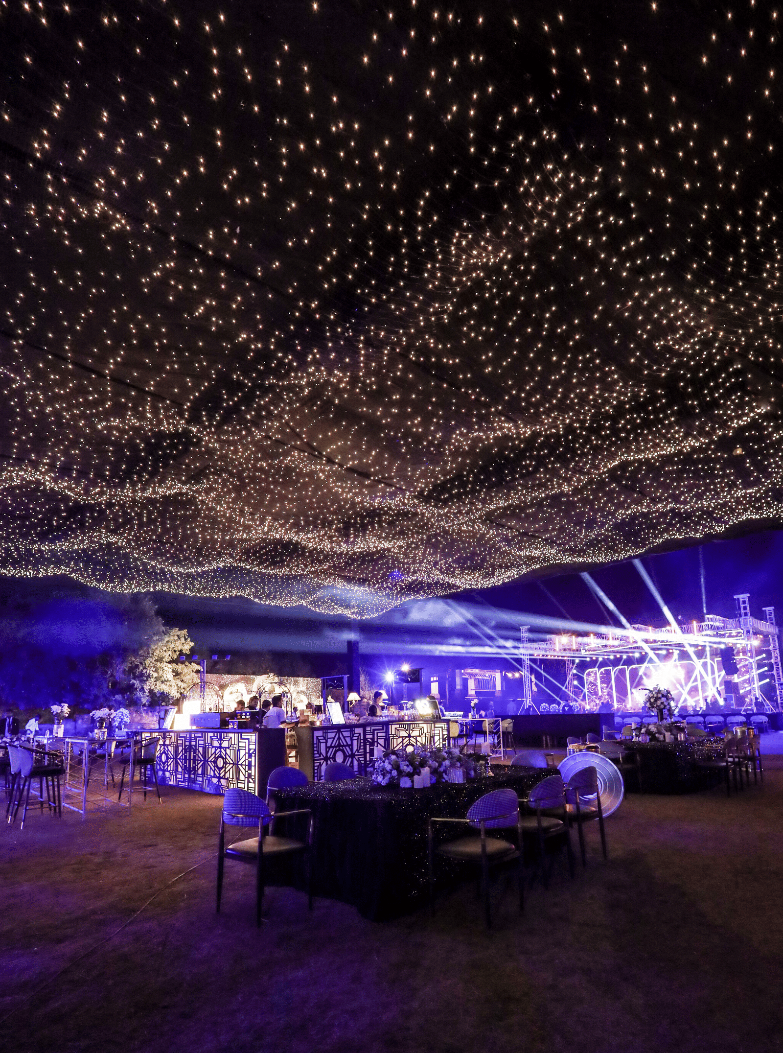 An enchanting night event setup at Ananta Spa & Resort, Jaipur, is covered by a wave-like ceiling canopy of warm fairy lights.