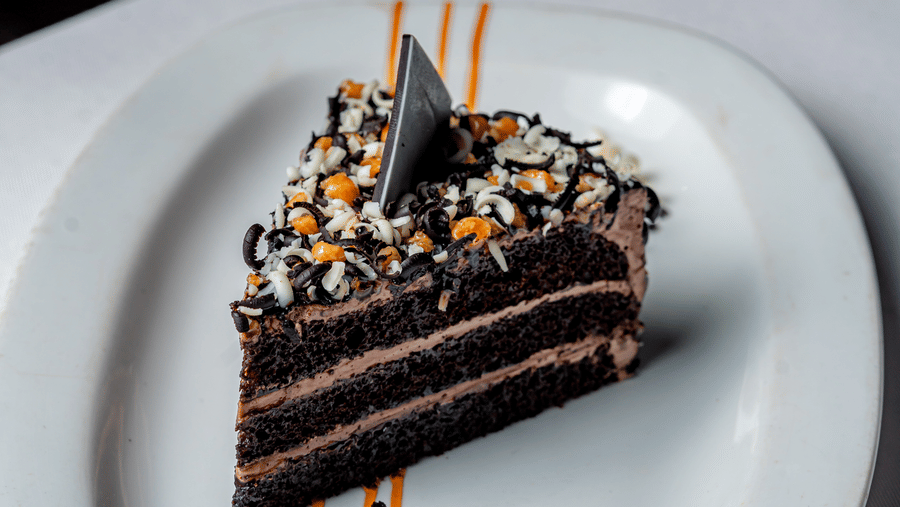 A slice of layered chocolate cake with sprinkles at Café Latte, part of the Noor-Us-Sabah Palace, Bhopal, served on a white plate with caramel drizzle.