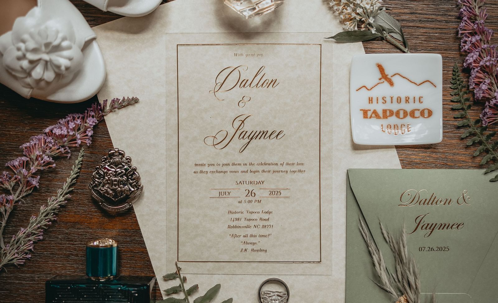 Wedding invitation cards of Dalton and Jaymee which took place on July 26, 2025 at the Historic Tapoco Lodge. They are placed on a table along with wedding rings, perfume bottles, bride's shoes, etc.