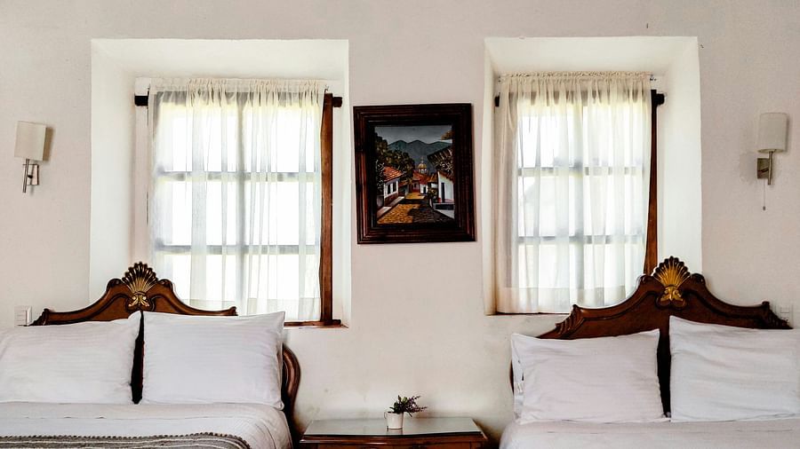A hotel room with twin beds, windows and a painting hanging on the wall.