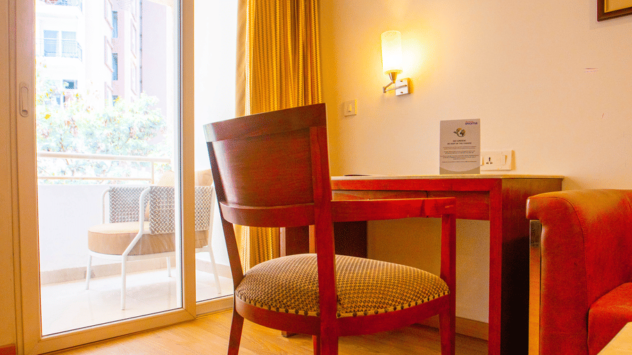 Hotel room seating nook at Featherlite Evoma Hotel with a wooden table and chairs beside a large window overlooking greenery outside it.