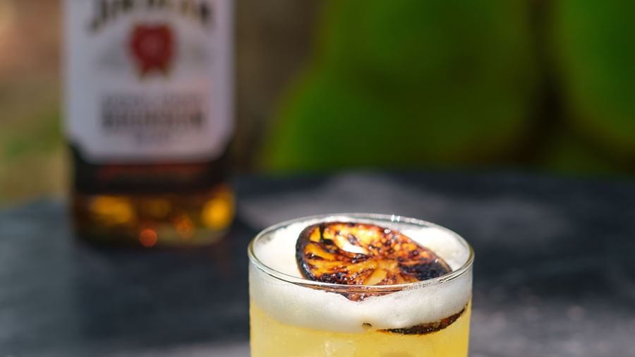 A glass of Whiskey Sour with a bottle of Jim Beam behind it | Mango Hill, Pondicherry