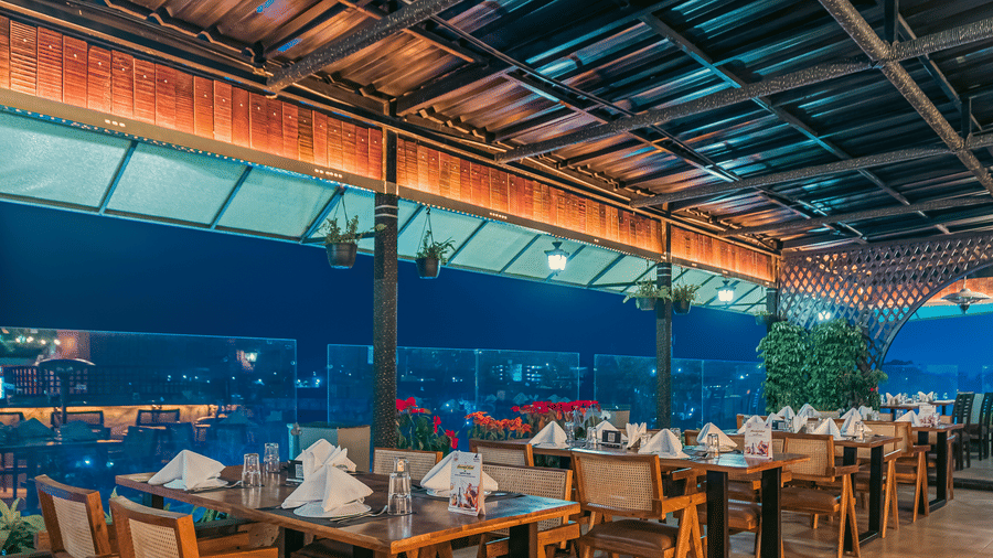 The Hills View restaurant at The Papaya Tree Hotels featuring an outdoor seating under a covered roof with wooden tables overlooking a scenic view, creating a relaxed open-air dining vibe.