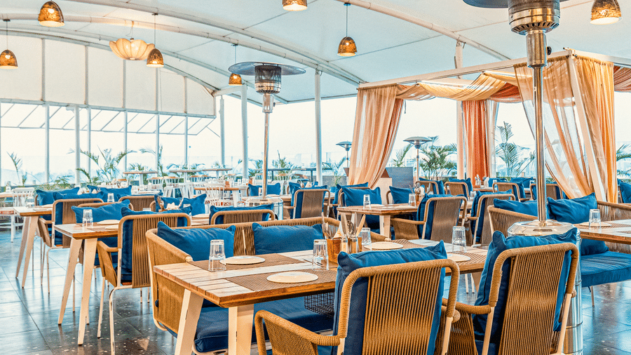 Bright dining space at The Papaya Tree Hotel’s Nazara restaurant featuring cushioned chairs, modern chandeliers, and large glass windows that fill the area with natural light.