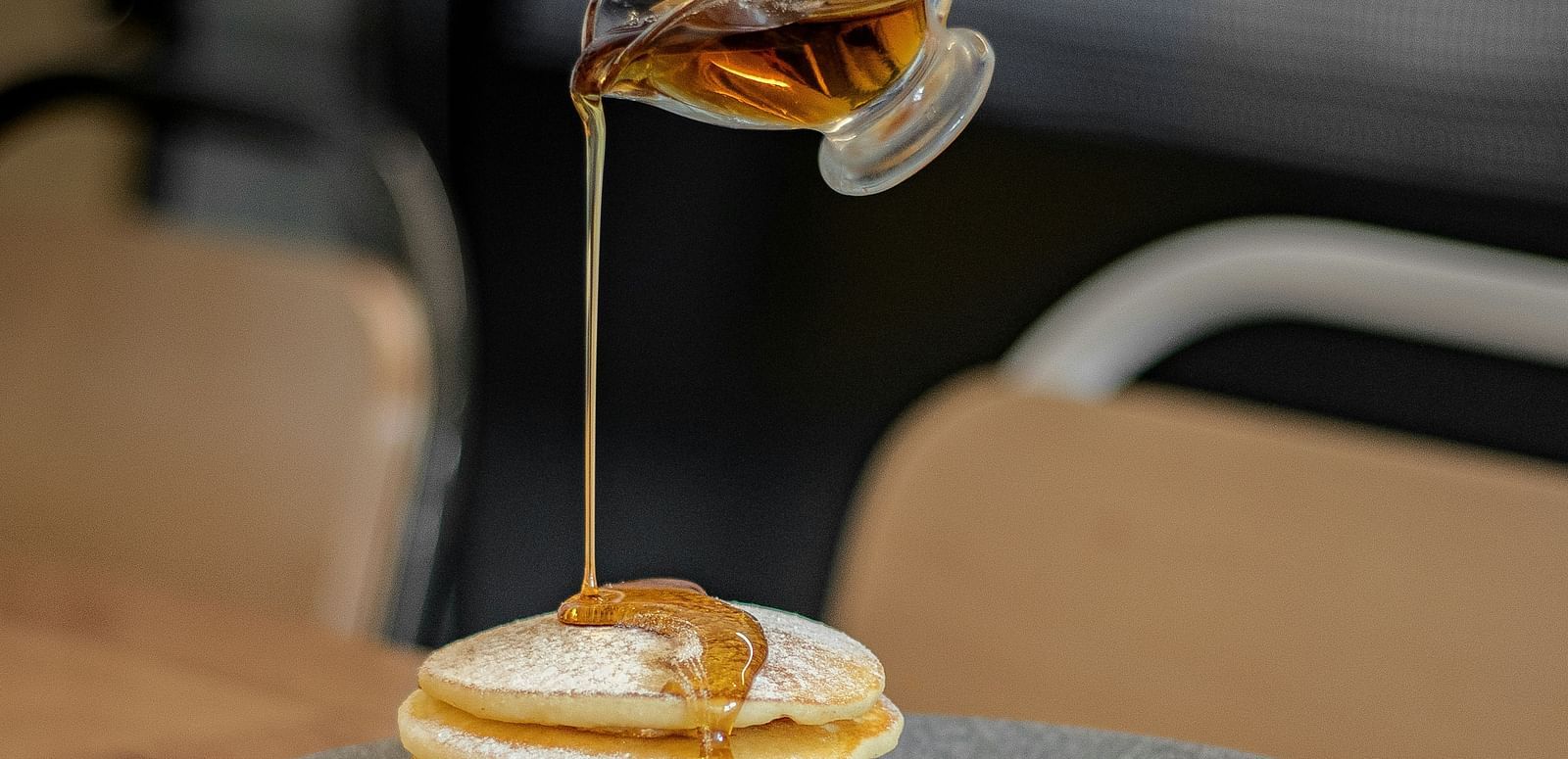 Honey being poured on a set of pancakes placed in a plate.