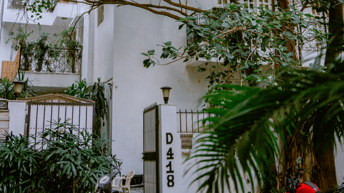 A charming exterior courtyard framed by cascading greenery and white colonial-style walls, offering a tranquil welcome to guests at Colonel’s Retreat, nestled in leafy surroundings.