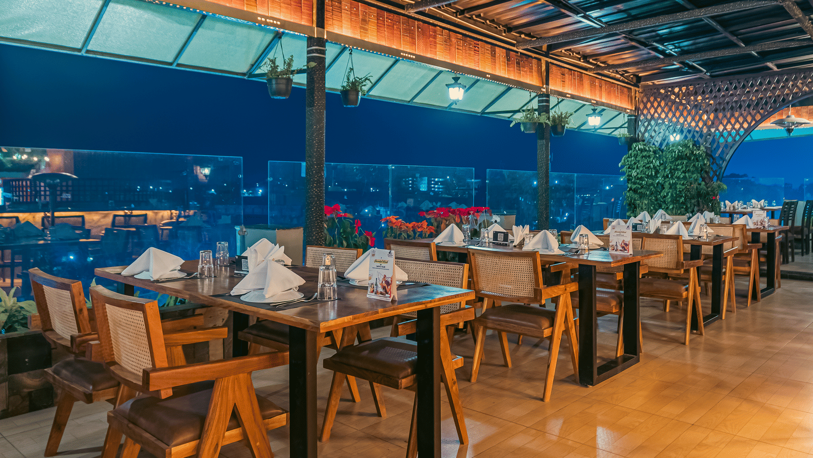 The Hills View restaurant at The Papaya Tree Hotels featuring an outdoor seating under a covered roof with wooden tables overlooking a scenic view, creating a relaxed open-air dining vibe.