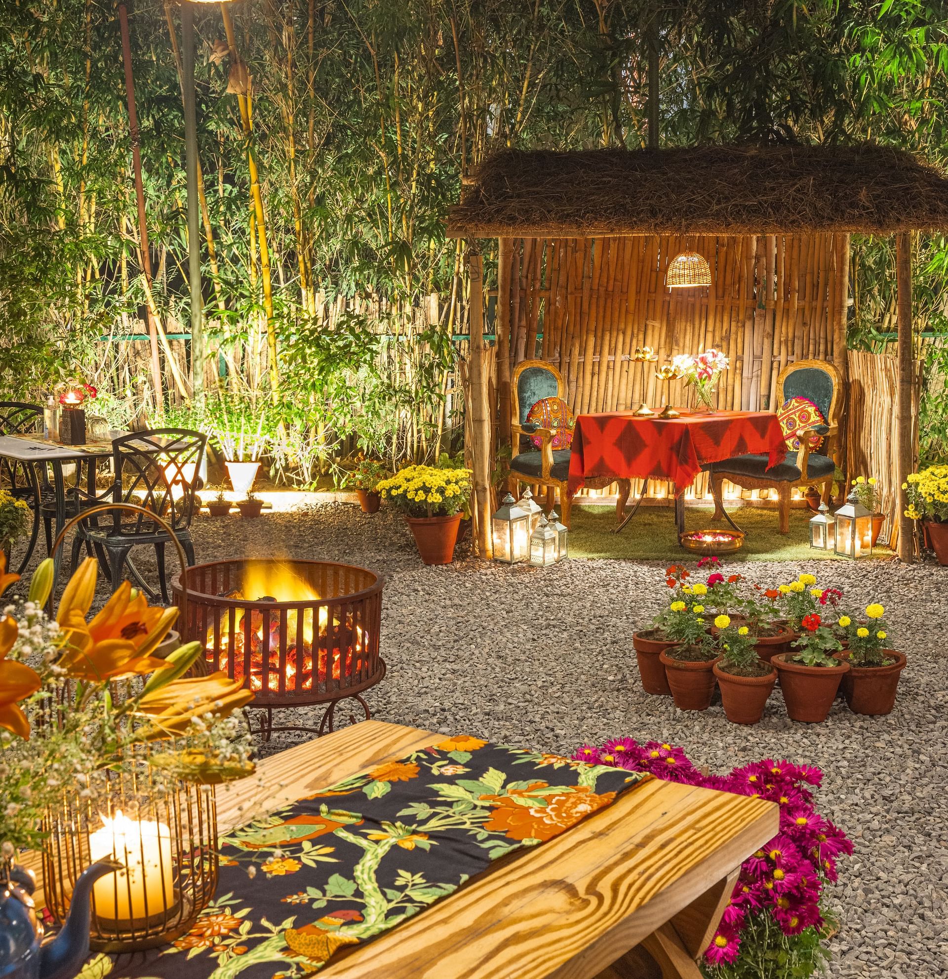 Charming outdoor dining area with warm lighting, colorful flowers, a wooden gazebo, and a table decorated with candles and a floral table runner - Karma Chalets