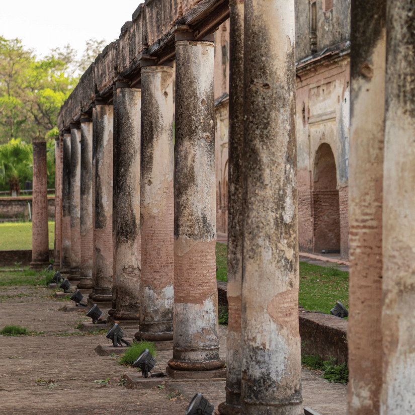 A close up shot of a series of pillars at The Residency, Lucknow. There is a pathway in front and the pillars are also lined with lights. There is trees visible at the far end.