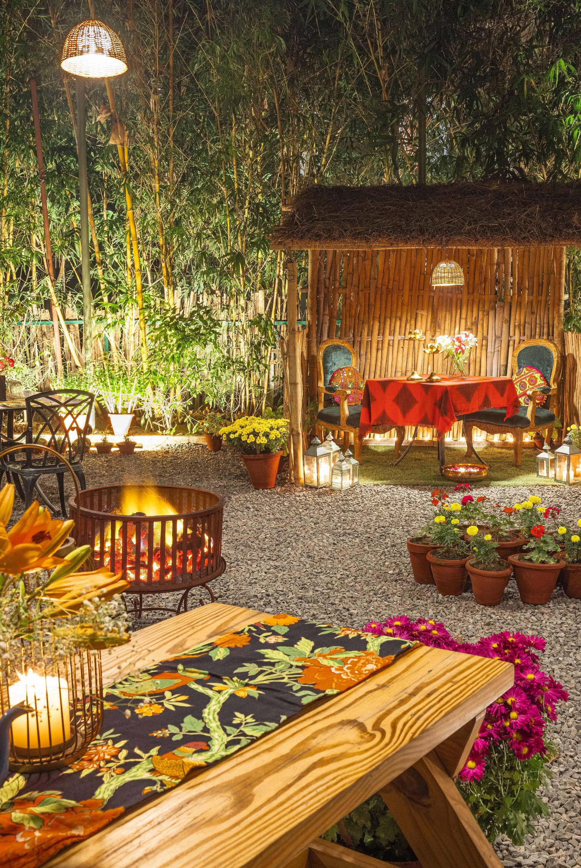 Charming outdoor dining area with warm lighting, colorful flowers, a wooden gazebo, and a table decorated with candles and a floral table runner - Karma Chalets