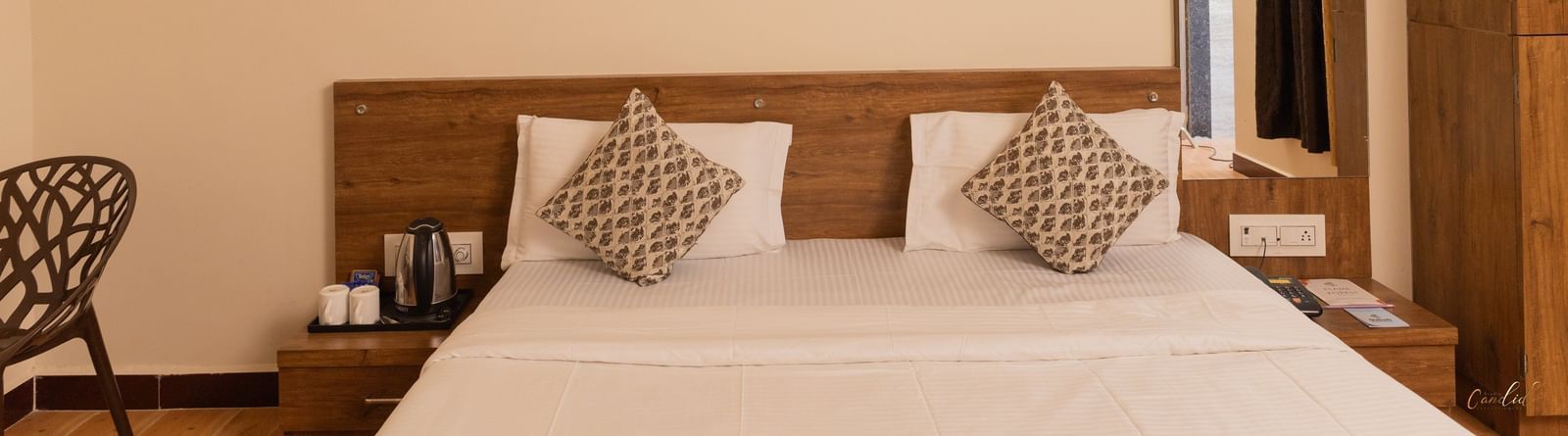 A close-up of a bed with brown accents, a wall art, a wall mirror, and a wooden wardrobe at Daksh Resort & Amusement Park, Sasan Gir.
