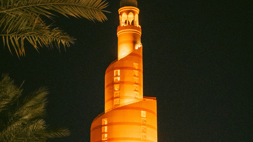 Night-time view of a spiral minaret tower illuminated in warm orange light against a dark sky.