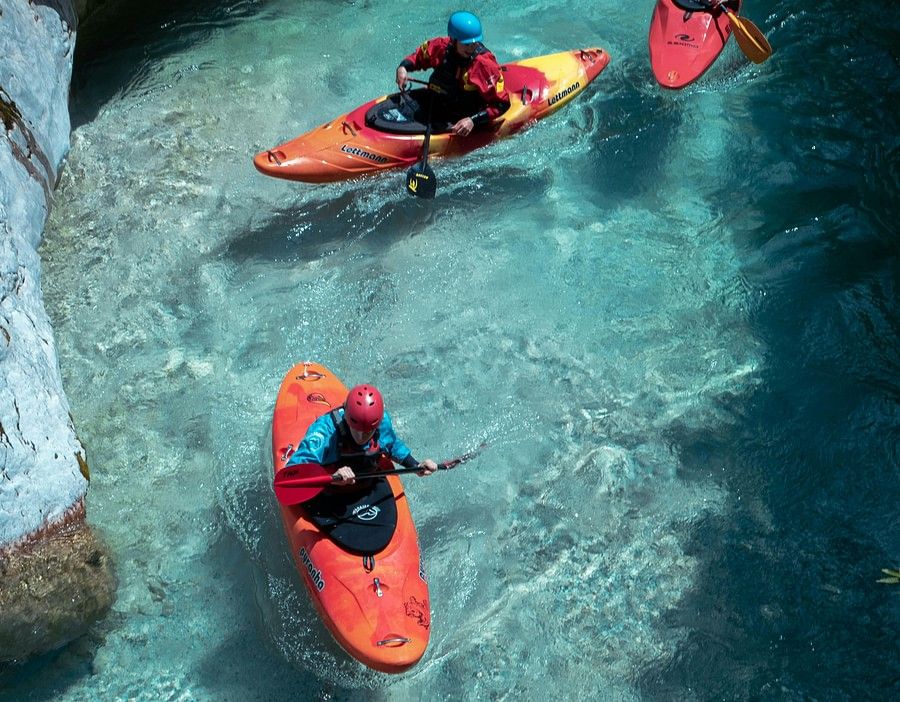 three kayakers on a narrow, blue water body, in between rocky walls.