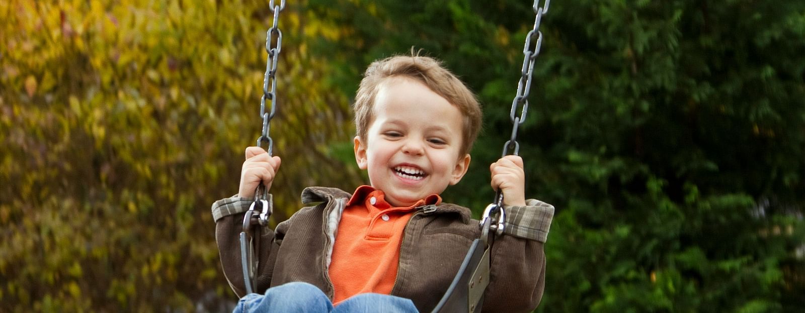 A child enjoying a swing with trees in the background.
