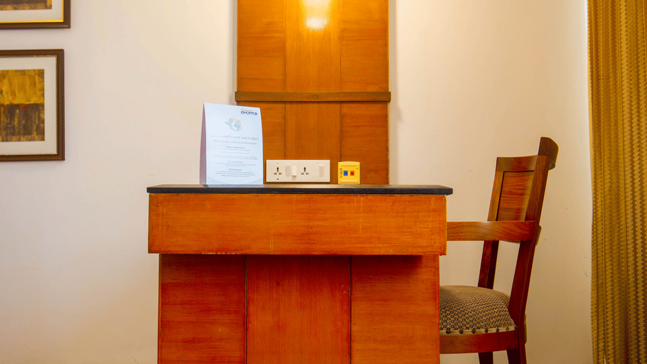 Hotel room desk area at Featherlite Evoma Hotel with a wooden writing desk, a chair and warm ambient lighting along the nearby wall.