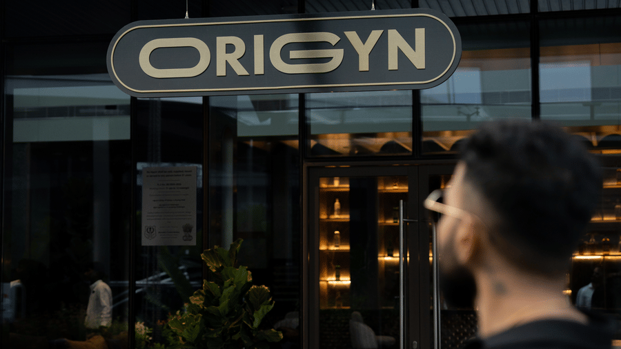 Person standing outside the entrance with Origyn signboard at Merlis Hotel, Coimbatore.
