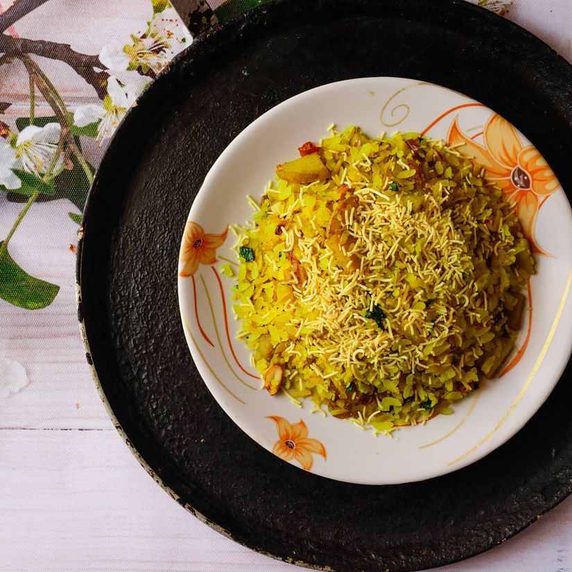 A plate of yellow rice with vegetables on a patterned tablecloth beside a black pan.