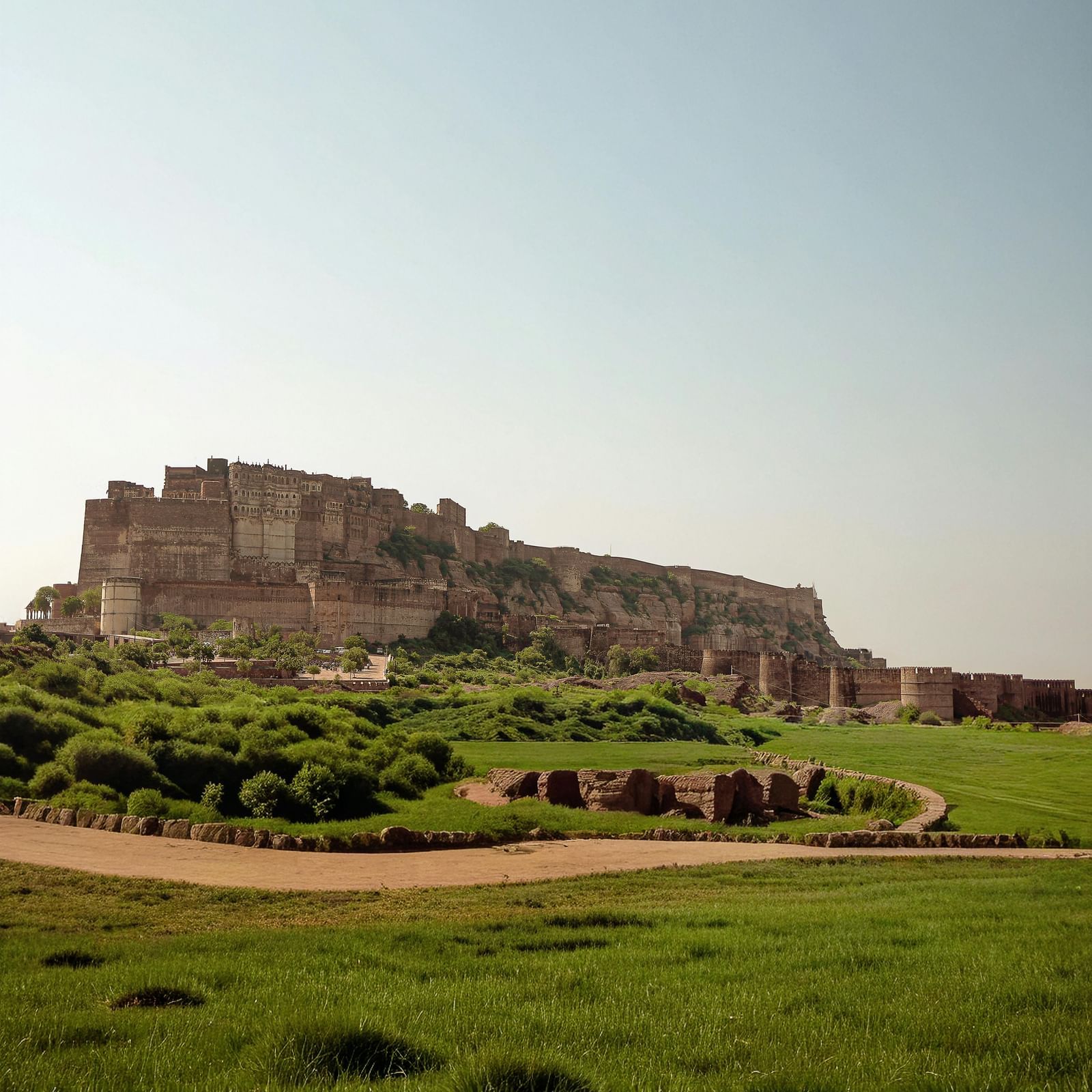 Historic fort atop a hill with surrounding green landscape and clear sky in the background.